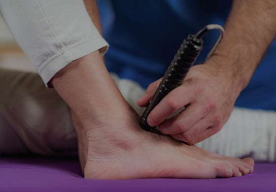 Close-up of male practitioner's hands as he uses the laser on the foot/ankle of a patient who is sitting up on a table