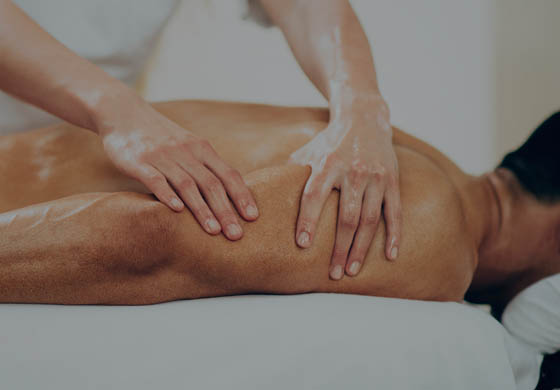 Therapist's hands work on the shoulder of a young, fit man who is lying face down on a massage table