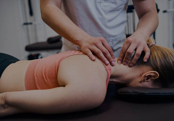 Young, male chiropractor works on the neck of a young, female patient who is lying face down on the table