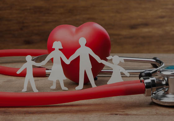 Red heart stress ball is in the middle with a family cut out of paper in front of it, a stethoscope is in the foreground