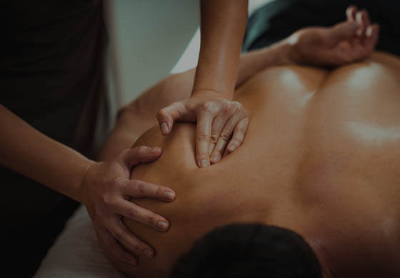 Young female massage therapist's hands work on the upper shoulder of an active male patient, who is laying face down on the table