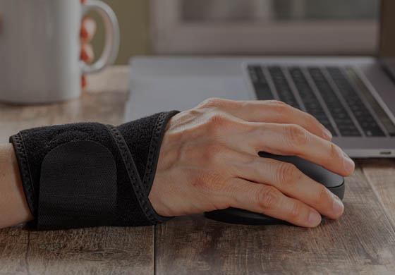 Man working at his laptop with a wrist brace on the hand reaching for the mouse