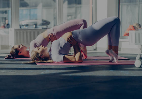 Two young, active women in a backbend completing pelvic exercises to strengthen their pelvic floor